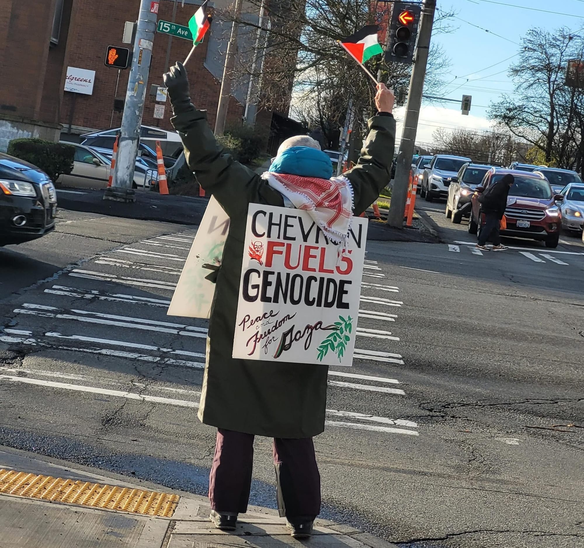 person waves Palestinian flags and holds placard with text chevron fuels genocide