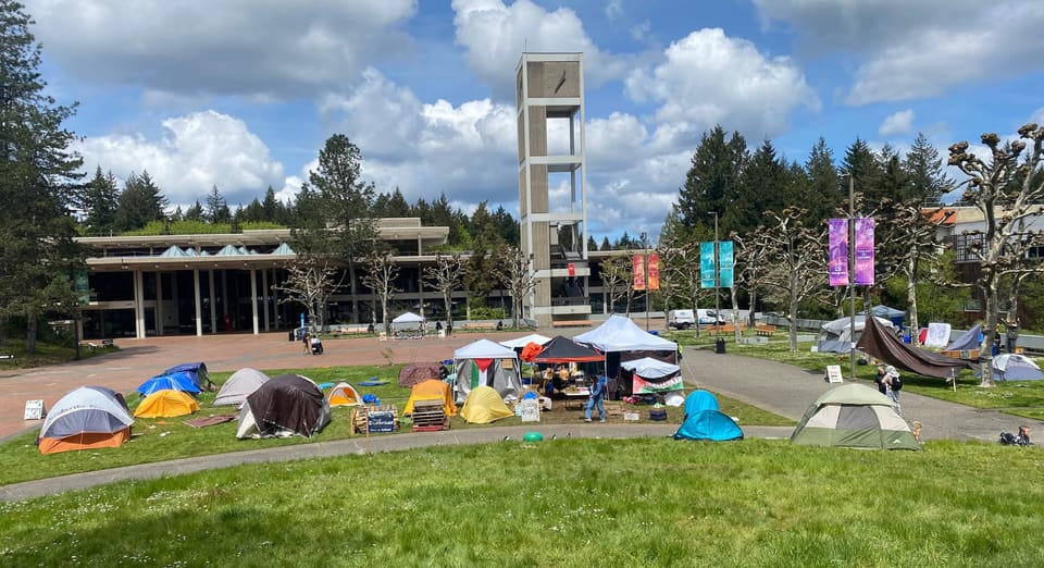 Tents pitched on grassy field with university buildings in the background